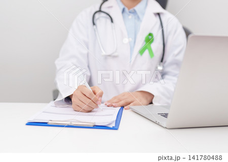 doctor using laptop and report notes on notebook. lime Green Ribbon for concept of May Celiac Awareness month, Lyme disease, September Lymphoma, Mental Health Awareness month and October Liver cancer 141780488