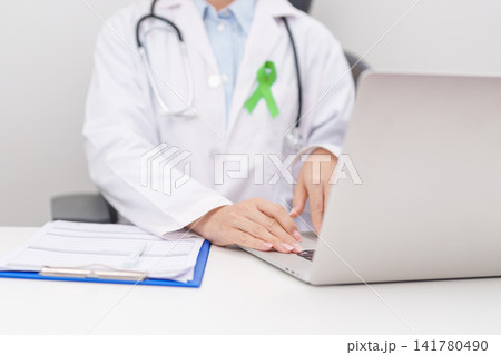 doctor using laptop and report notes on notebook. lime Green Ribbon for concept of May Celiac Awareness month, Lyme disease, September Lymphoma, Mental Health Awareness month and October Liver cancer doctor using laptop and report notes on notebook. lime Green Ribbon for concept of May Celiac Awareness month, Lyme disease, September Lymphoma, Mental Health Awareness month and October Liver cancer 141780490