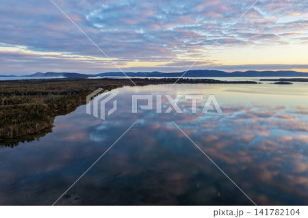 Aerial view of soft pastel clouds reflected across the calm waters of Pipers Bay, creating a peaceful coastal scene with gentle colours, still conditions and a tranquil natural atmosphere. Aerial view of soft pastel clouds reflected across the calm waters of Pipers Bay, creating a peaceful coastal scene with gentle colours, still conditions and a tranquil natural atmosphere. 141782104