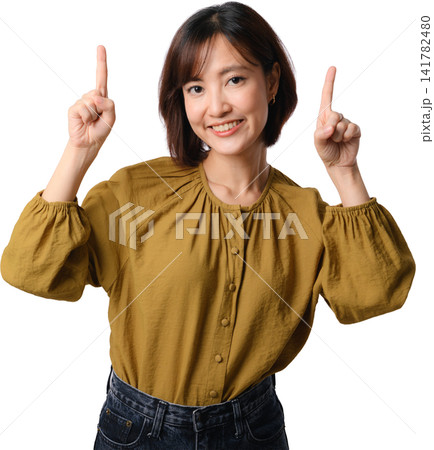 Smiling Asian woman pointing upward in mustard blouse isolated on transparent background with positive expression and copy space 141782480
