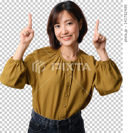 Smiling Asian woman pointing upward in mustard blouse isolated on transparent background with positive expression and copy space 141782480