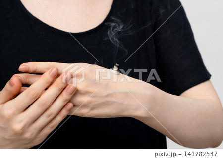 手の甲で煙を上げる台座灸と添えた女性の指 手の甲で煙を上げる台座灸と添えた女性の指 141782537