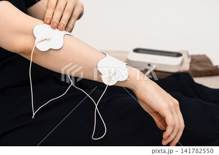 前腕に低周波治療器の電極パッドを貼る女性 前腕に低周波治療器の電極パッドを貼る女性 141782550