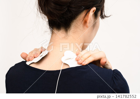 首と肩の境目に電極パッドを貼る女性の後ろ姿 首と肩の境目に電極パッドを貼る女性の後ろ姿 141782552