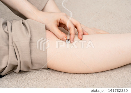 女性のすねで煙を上げる台座灸へ手を添える脚 女性のすねで煙を上げる台座灸へ手を添える脚 141782880