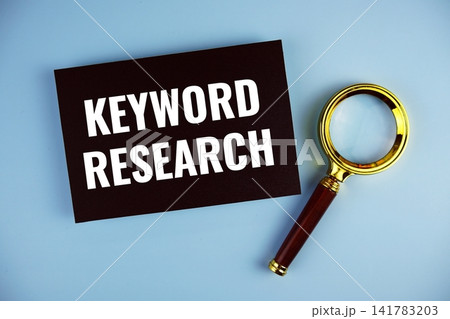 Keyword Research text written on paper card with magnifying glass top view on blue background 141783203