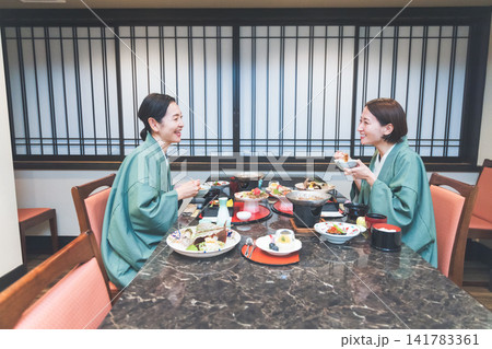 温泉旅館のお食事処で豪華な和会席を楽しむ浴衣姿の女性二人 温泉旅館のお食事処で豪華な和会席を楽しむ浴衣姿の女性二人 141783361