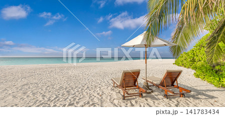 Romantic beach loungers under palm tree with parasol on powdery sand beside turquoise sea blue sky tropical shore. Perfect summer honeymoon travel paradise. Luxury couples getaway relax scenic 141783434