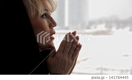 Mature woman finding solace and spiritual peace while praying with folded hands, reflecting devotion, contemplation, and hope in a moment of quiet personal worship Mature woman finding solace and spiritual peace while praying with folded hands, reflecting devotion, contemplation, and hope in a moment of quiet personal worship 141784445