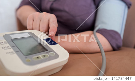 Senior woman checking blood pressure at home with a digital tonometer on her arm, emphasizing self care, prevention, daily monitoring and independent health management 141784447