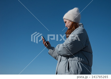 Young woman texting on smartphone against blue sky 141785265