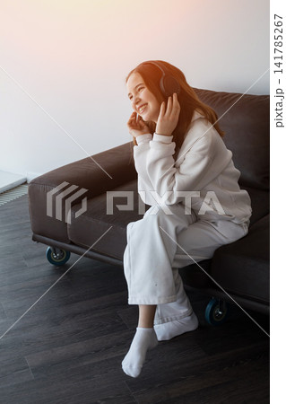 Happy teen girl enjoying music with headphones on couch Happy teen girl enjoying music with headphones on couch 141785267