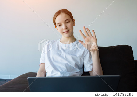 Young woman waving hello during video call from home Young woman waving hello during video call from home 141785299