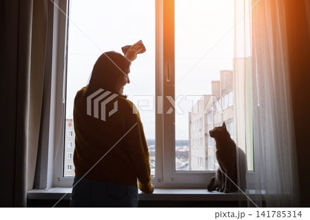 Pregnant woman standing by a bright window with city view, hand on belly and calm morning light Pregnant woman standing by a bright window with city view, hand on belly and calm morning light 141785314