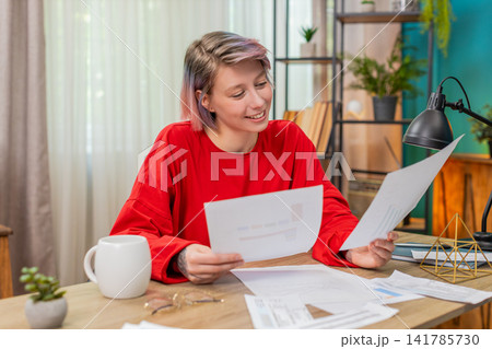 Young woman happily reviewing financial documents, nodding positively satisfied, successful results Young woman happily reviewing financial documents, nodding positively satisfied, successful results 141785730