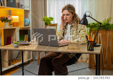Young woman on home table sees bad news on laptop feeling upset after online game loss or rejection Young woman on home table sees bad news on laptop feeling upset after online game loss or rejection 141785765