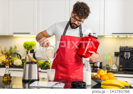 Arabian young adult man pours whey protein smoothie into glass and drinks after workout in kitchen 141785766