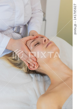 Woman having relaxing forehead massage procedure by professional beautician in cosmetology clinic Woman having relaxing forehead massage procedure by professional beautician in cosmetology clinic 141785827