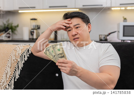 Asian man checks wallet sees only small dollar bills frowns and sets saving goal for budget plan new 141785838