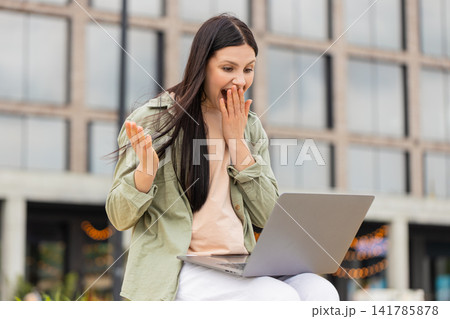 Young woman celebrating good news walking in city street with laptop and showing happy success joy Young woman celebrating good news walking in city street with laptop and showing happy success joy 141785878