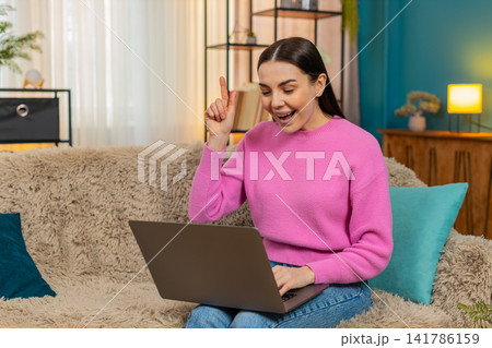 Young woman sitting on sofa working on laptop searching solution excitedly shouting Eureka with joy Young woman sitting on sofa working on laptop searching solution excitedly shouting Eureka with joy 141786159