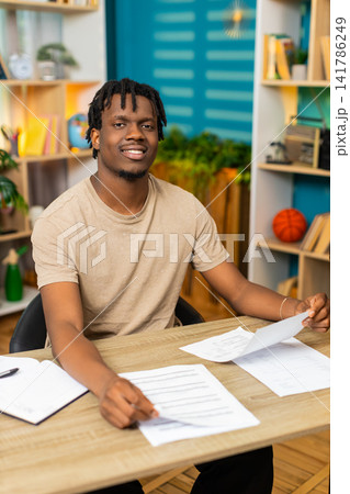 African American young man on home table organizing paperwork carefully into neat stack at home desk African American young man on home table organizing paperwork carefully into neat stack at home desk 141786249
