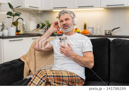 Middle-aged man turns on playlist in headphones nods to beat smiles relax takes break from work calm Middle-aged man turns on playlist in headphones nods to beat smiles relax takes break from work calm 141786289