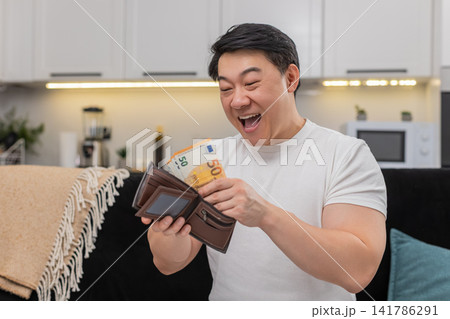 Asian man holds cash euros as fan laughs shows victory sign puts money into wallet after count win 141786291