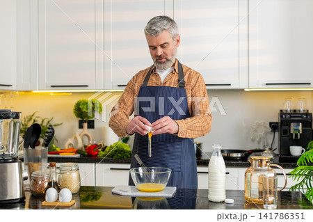 Middle-aged man smiling cracking eggs whisking mixture in home kitchen for diet nutrition meal prep Middle-aged man smiling cracking eggs whisking mixture in home kitchen for diet nutrition meal prep 141786351