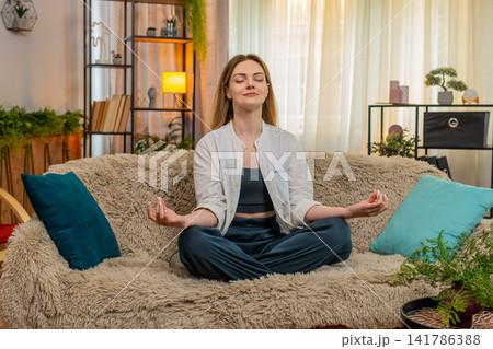 Woman meditating peacefully on home sofa, calm expression, eyes closed, relaxation, taking a break Woman meditating peacefully on home sofa, calm expression, eyes closed, relaxation, taking a break 141786388