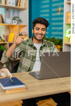 Indian man on home table explaining business idea on laptop video call with confident smile for work Indian man on home table explaining business idea on laptop video call with confident smile for work 141786447