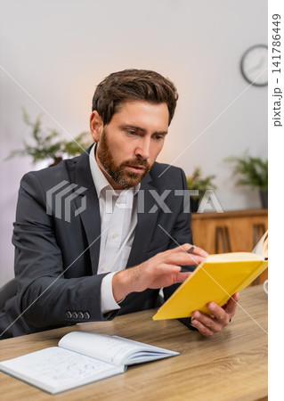 Middle-aged businessman studies guide leadership smiles at quote writes idea in notebook motivated Middle-aged businessman studies guide leadership smiles at quote writes idea in notebook motivated 141786449