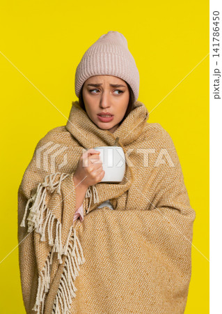 Woman wrapped in blanket wearing hat adding honey to tea slowly drinking caring for sore throat Woman wrapped in blanket wearing hat adding honey to tea slowly drinking caring for sore throat 141786450
