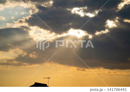 夕暮れの暗い雲間から屋根の上へ差し込む劇的な光芒 141786491