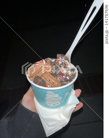 Swirled yogurt ice cream dessert served in a cup, smooth creamy texture with glossy surface, topped with fresh fruit pieces, highlighting its refreshing and inviting appearance in detail 141787696