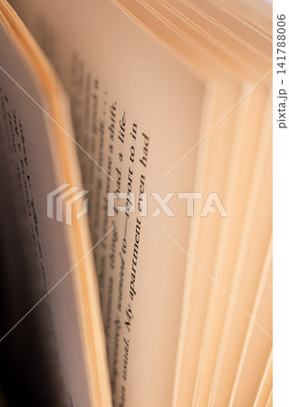 Close-up view of open book pages with visible blurred text and soft lighting. The pages are slightly curled, showcasing the texture and color of the paper. Close-up view of open book pages with visible blurred text and soft lighting. The pages are slightly curled, showcasing the texture and color of the paper. 141788006
