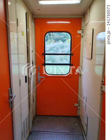 Bright orange exit door inside a passenger train carriage with window view of motion landscape Bright orange exit door inside a passenger train carriage with window view of motion landscape 141788073