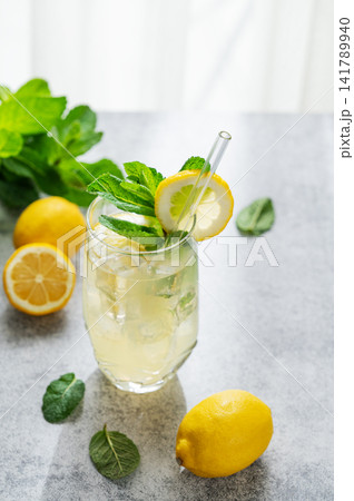 A summer drink with lemon, mint, and ice in a two glasses against a sunny window background. 141789940