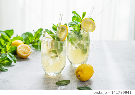 A summer drink with lemon, mint, and ice in a two glasses against a sunny window background. 141789941