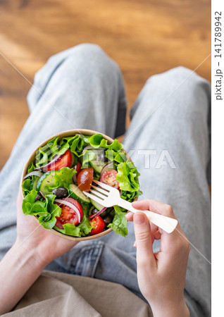 A woman holds a healthy vegetable salad in an eco-friendly takeaway bowl. A woman holds a healthy vegetable salad in an eco-friendly takeaway bowl. 141789942