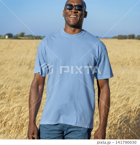 Blank blue t-shirt mockup on black man in wheat field at sunset, front view with copy space Blank blue t-shirt mockup on black man in wheat field at sunset, front view with copy space 141790030