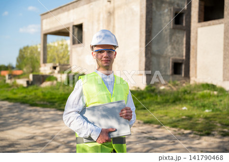 Engineer with laptop standing on a residential building site under construction. Construction profession urban development and site survey Engineer with laptop standing on a residential building site under construction. Construction profession urban development and site survey 141790468