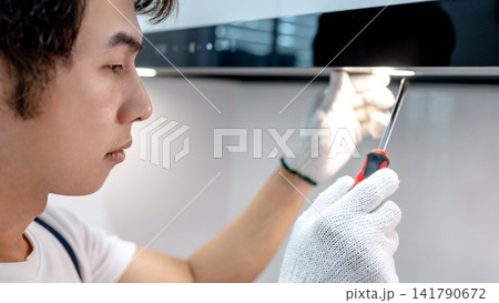 Asian male maintenance worker using screwdriver fixing light on cooker hood Asian male maintenance worker using screwdriver fixing light on cooker hood 141790672