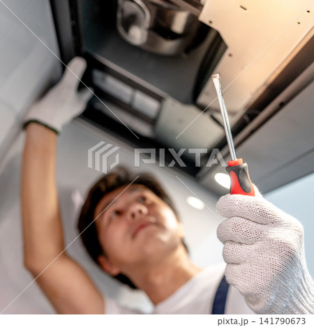 Asian male technician using screwdriver fixing extractor motor in cooker hood Asian male technician using screwdriver fixing extractor motor in cooker hood 141790673