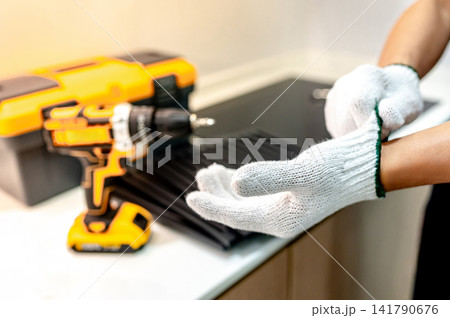 Male hand of maintenance worker putting on protective gloves near electric screwdriver and toolbox 141790676