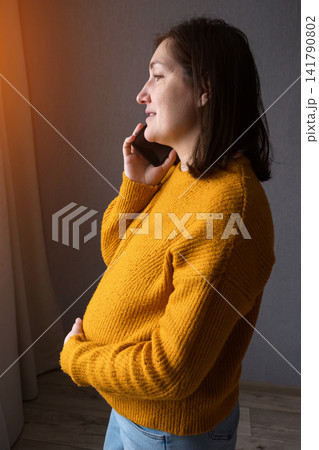 Pregnant woman holding a phone and smiling in a warm indoor setting Pregnant woman holding a phone and smiling in a warm indoor setting 141790802