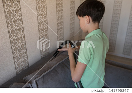 Young boy vacuuming sofa practicing household chores Young boy vacuuming sofa practicing household chores 141790847