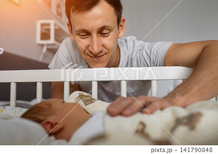 Father looking at baby sleeping peacefully in crib Father looking at baby sleeping peacefully in crib 141790848