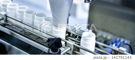 Automatic white plastic bottle filling machine working on conveyor belt line in pharmaceutical factory Automatic white plastic bottle filling machine working on conveyor belt line in pharmaceutical factory 141791143