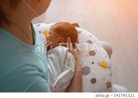 Mother breastfeeding newborn baby using a nursing pillow for comfort 141791321